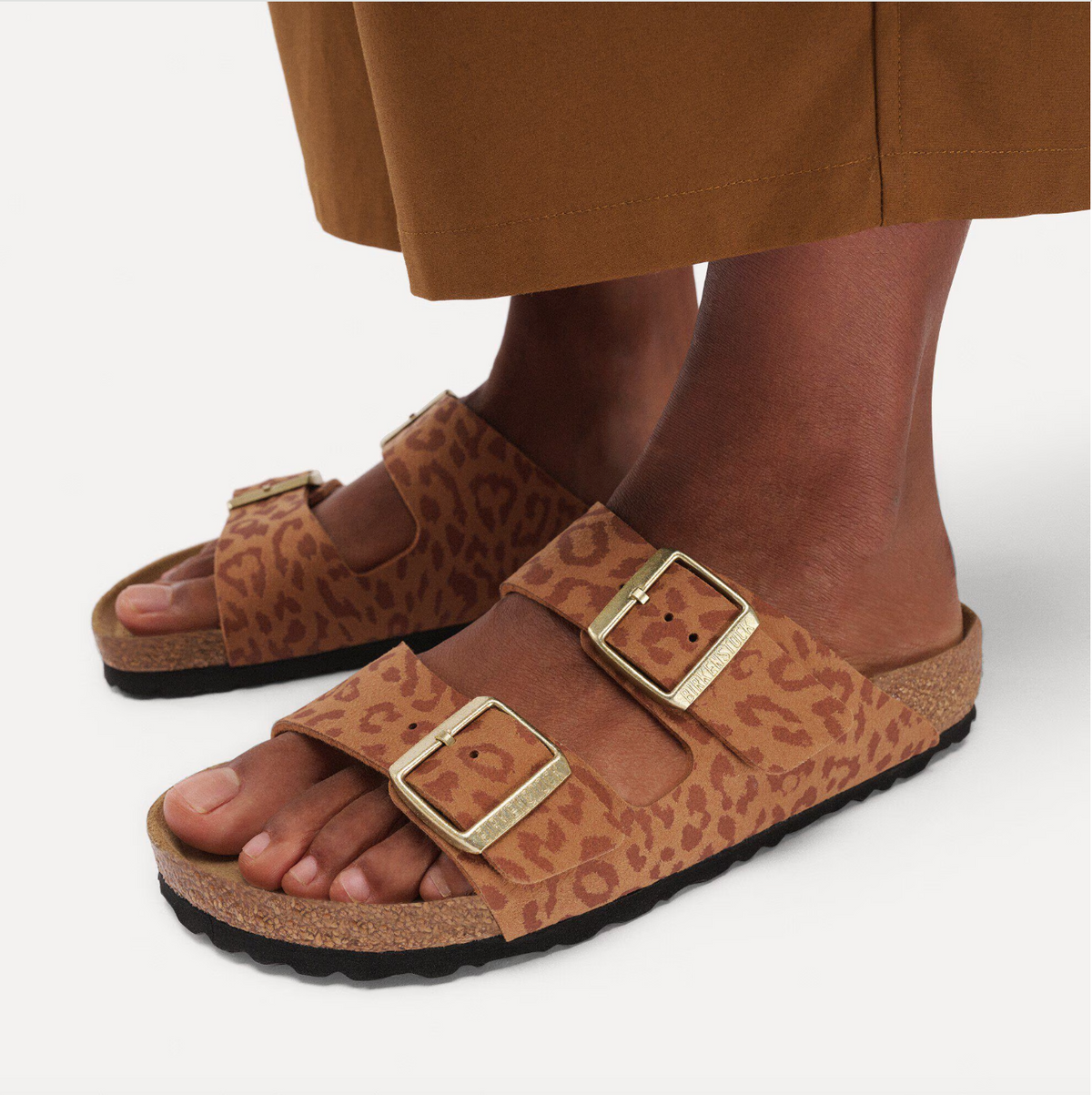 Pair of leopard print Birkenstock Arizona sandals with gold buckles worn by model