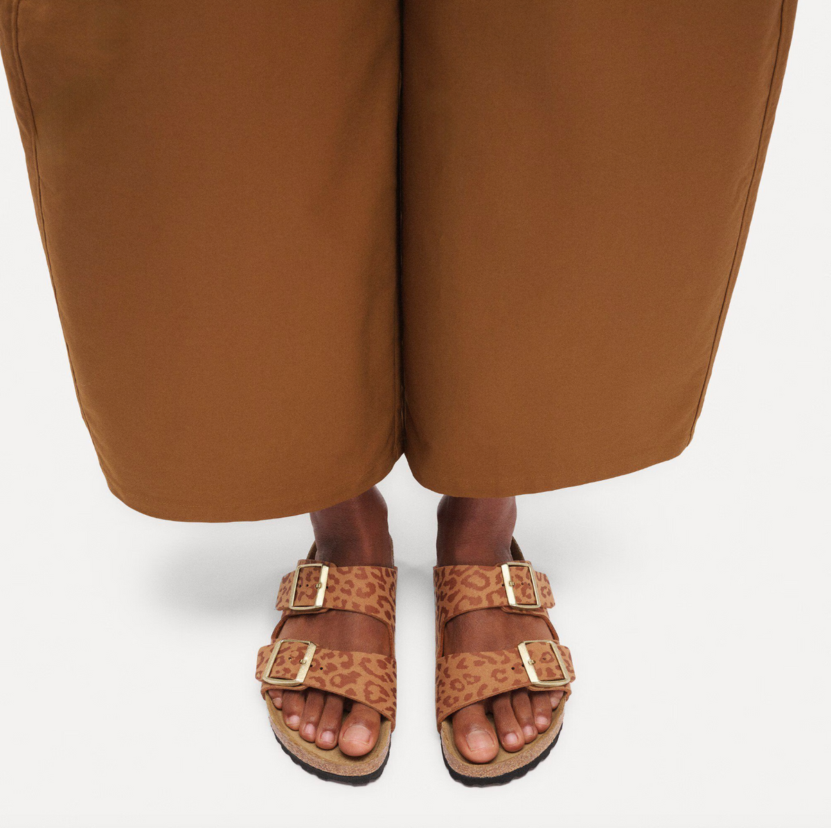 Pair of leopard print Birkenstock Arizona sandals with gold buckles worn by model