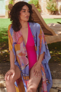 Model wears a One Hundred Stars Giant Crane Throwover in bright pinks and lilac over a swimsuit. Available at theshoegallery.co.uk
