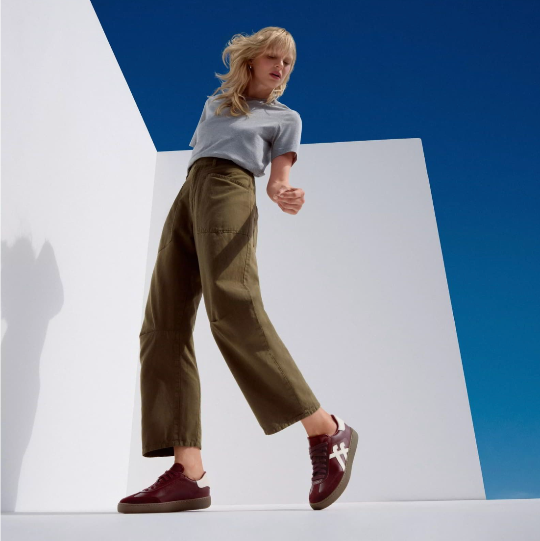 Model wears FitFlop Dash Trainer  in dark merlot leather with suede toe and cream toned fitflop branding on the side and at the heel.
