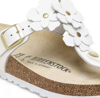 Close-up of a white sandal with floral details and 'Birkenstock' branding on a white background.