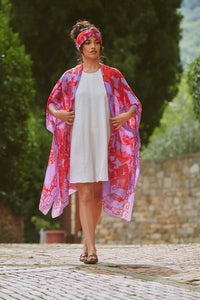 Model wears a One Hundred Stars Giant Willow Throwover in bright red and lilac over a white dress. Available at theshoegallery.co.uk