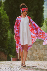 Model wears a One Hundred Stars Giant Willow Throwover in bright red and lilac over a white dress. Available at theshoegallery.co.uk