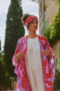 Model wears a One Hundred Stars Giant Willow Throwover in bright red and lilac over a white dress. Available at theshoegallery.co.uk