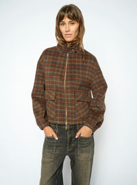 A model wearing a Mos Mosh brown and orange plaid zip-up jacket with a high collar, paired with dark grey jeans, against a plain light grey background.