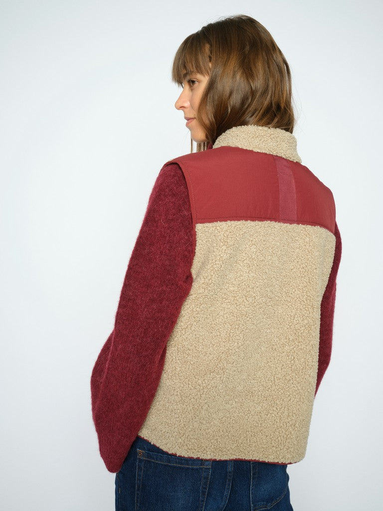 Model wears a sleeveless Mos Mosh zip-front vest in beige teddy trimmed with burgundy 