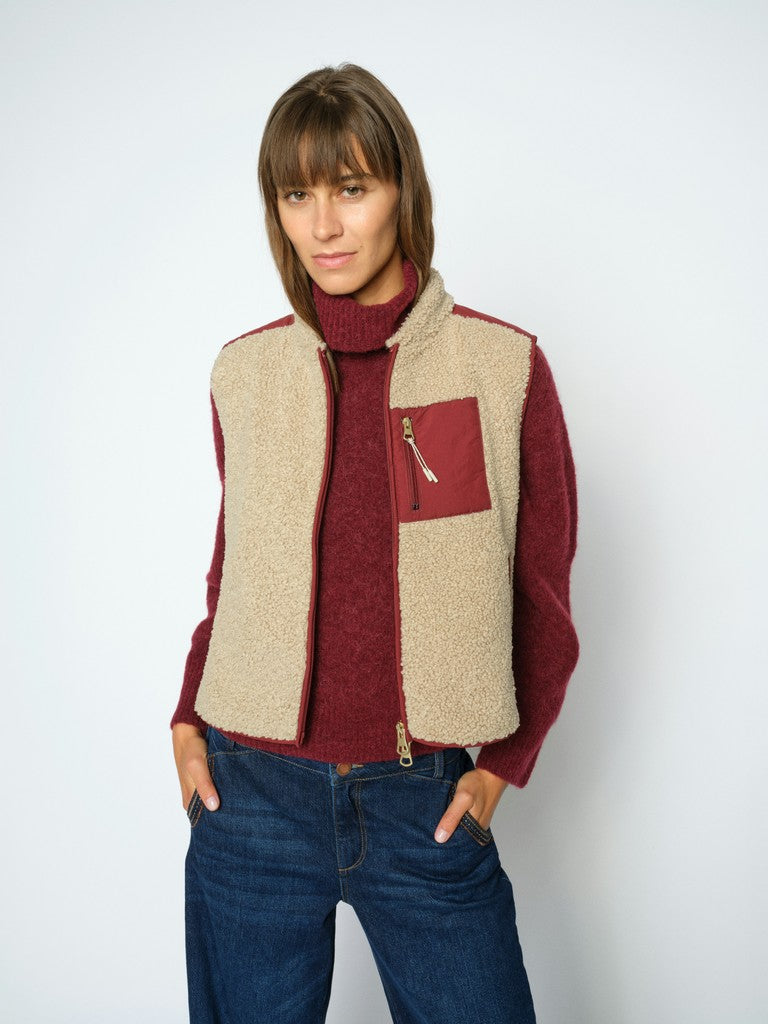 Model wears a sleeveless Mos Mosh zip-front vest in beige teddy trimmed with burgundy 
