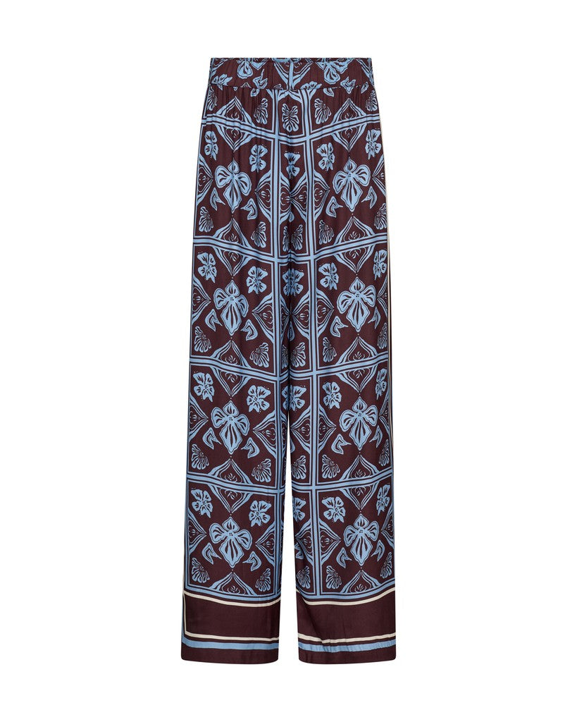 Mos Mosh wide-leg pants featuring a dark brown base with a light blue and white geometric and floral block print pattern, shown against a plain white background.