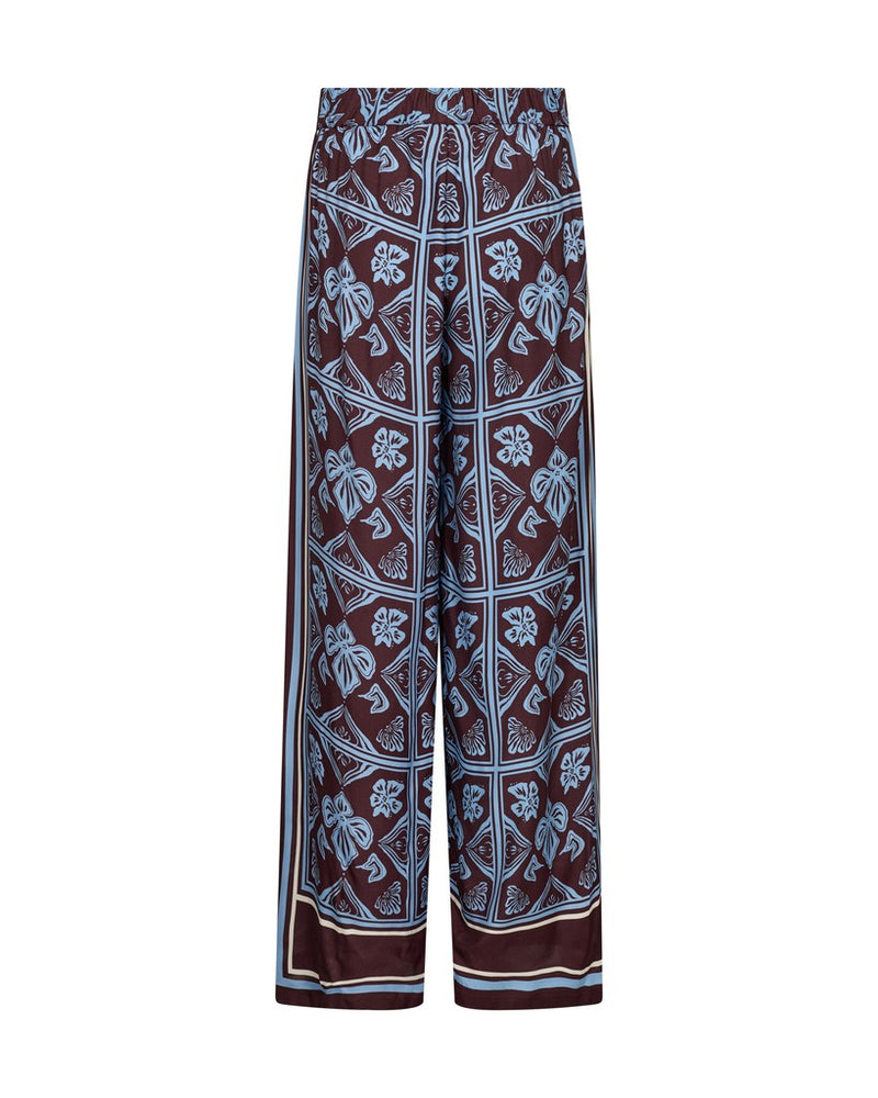 Mos Mosh wide-leg pants featuring a dark brown base with a light blue and white geometric and floral block print pattern, shown against a plain white background.