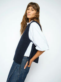Model wears a dark navy blue Mos Mosh knit sweater vest over a white short-sleeve button-up shirt and dark blue wide-leg trousers