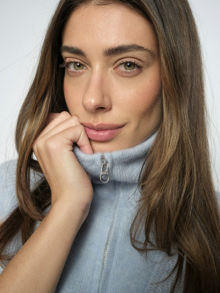 Model wears a pale blue Mos Mosh sleeveless sweater with zipped high neck 
