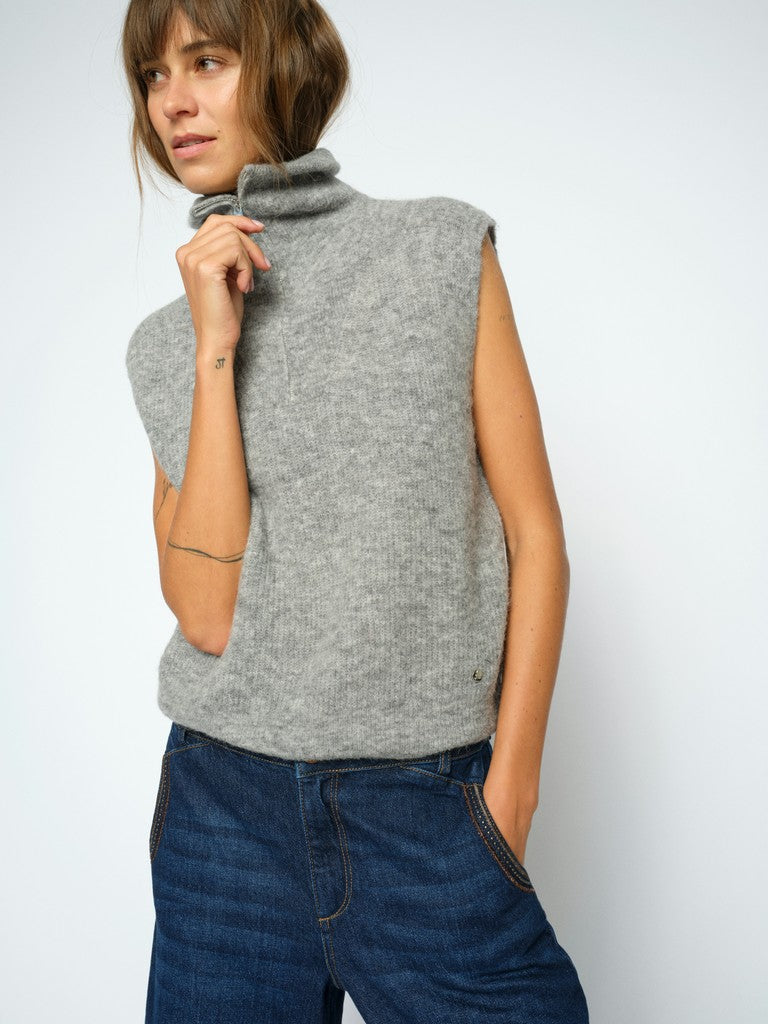 Model wears a light grey Mos Mosh ribbed knit sleeveless turtleneck sweater vest, paired with blue jeans