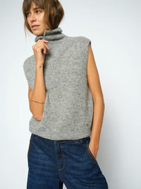 Model wears a light grey Mos Mosh ribbed knit sleeveless turtleneck sweater vest, paired with blue jeans