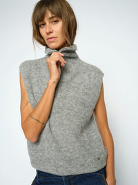 Model wears a light grey Mos Mosh ribbed knit sleeveless turtleneck sweater vest, paired with blue jeans