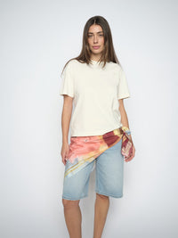 Woman wearing a cream t-shirt and denim shorts with a colorful scarf on a white background