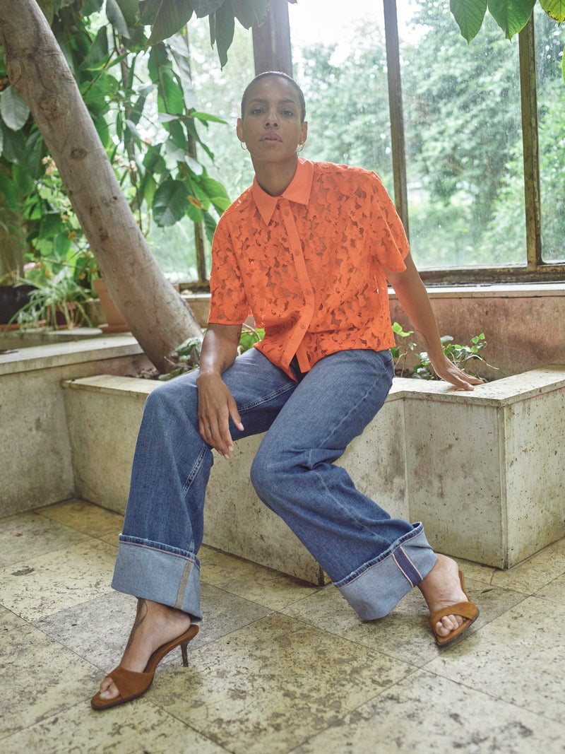 model is wearing a vibrant orange lace shirt with collar paired with denim jeans