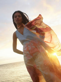 Woman standing on a beach with a colorful scarf, sunset in the background