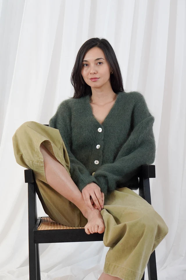 Model wears the TWNS Malia V Neck Cardigan in Military Green which has a cosy luxe vibe. It has a relaxed shape with pearlised buttons.