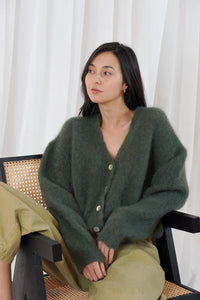 Model wears the TWNS Malia V Neck Cardigan in Military Green which has a cosy luxe vibe. It has a relaxed shape with pearlised buttons.