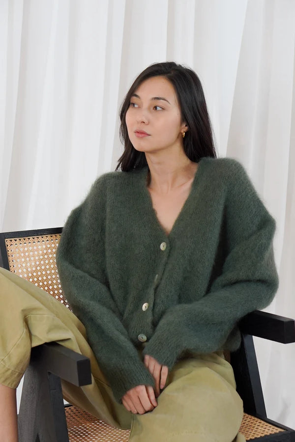 Model wears the TWNS Malia V Neck Cardigan in Military Green which has a cosy luxe vibe. It has a relaxed shape with pearlised buttons.