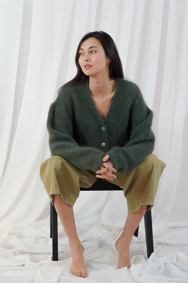 Model wears the TWNS Malia V Neck Cardigan in Military Green which has a cosy luxe vibe. It has a relaxed shape with pearlised buttons.
