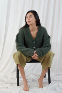 Model wears the TWNS Malia V Neck Cardigan in Military Green which has a cosy luxe vibe. It has a relaxed shape with pearlised buttons.