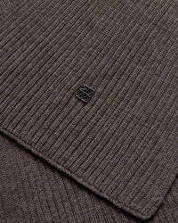 Close-up of the mole brown ribbed wool knit Mos Mosh Scarf with a small logo charm in the centre