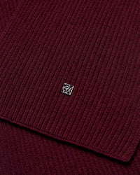 Close-up of the dark burgundy ribbed wool knit Mos Mosh Scarf with a small logo charm in the centre