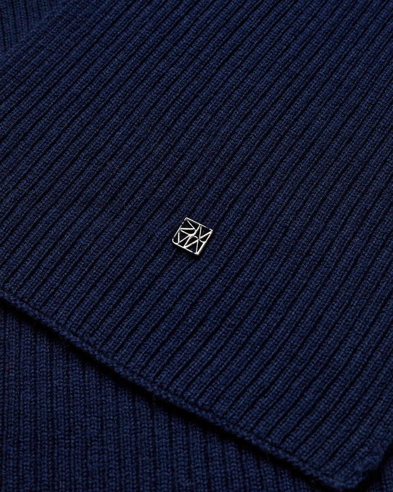 Close-up of the dark navy ribbed wool knit Mos Mosh Scarf with a small logo charm in the center.