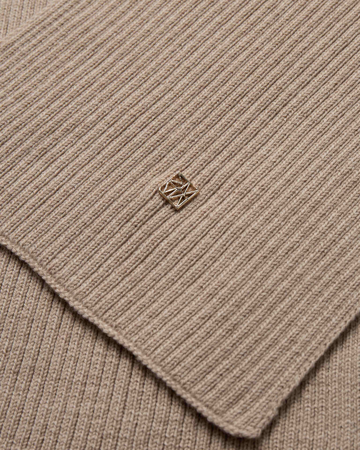 Close-up of the beige ribbed wool knit Mos Mosh Scarf with a small logo charm in the centre.