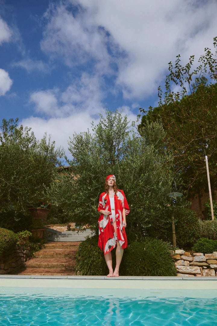 Model wears the Stork Red Throwover by One Hundred Stars available at The SHOE GALLERY over a white swimsuit