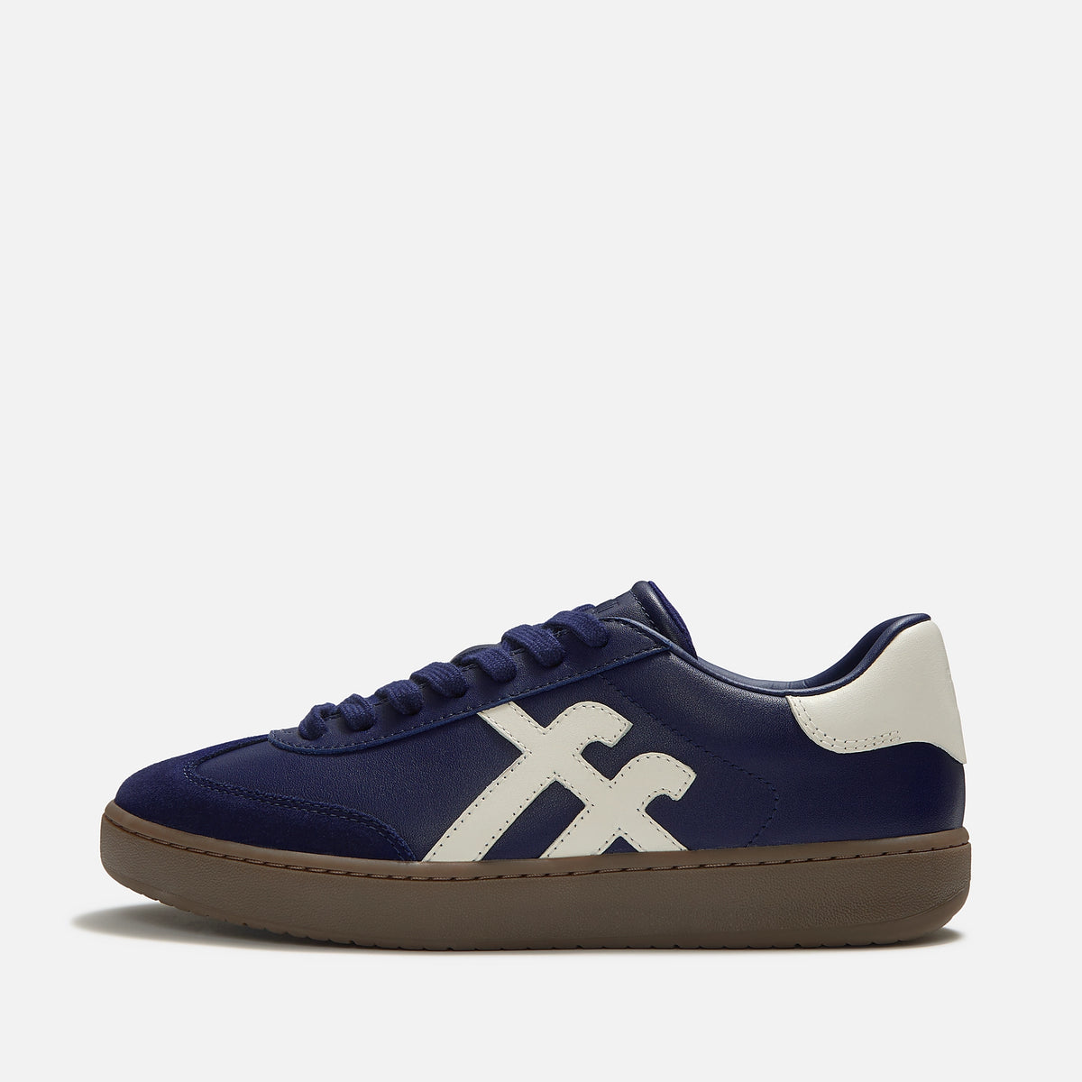 A close-up of FitFlop Dash navy blue suede and leather sneaker with matching navy laces, a white side stripe, and a brown gum sole, available at The hoe Gallery