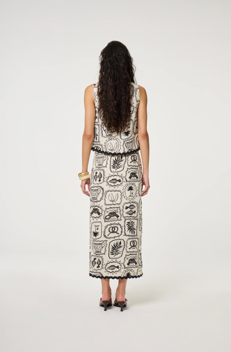 Models wears a wrap style skirt in black and white tile pattern edged with black rick rack by Fabienne Chapot, back view