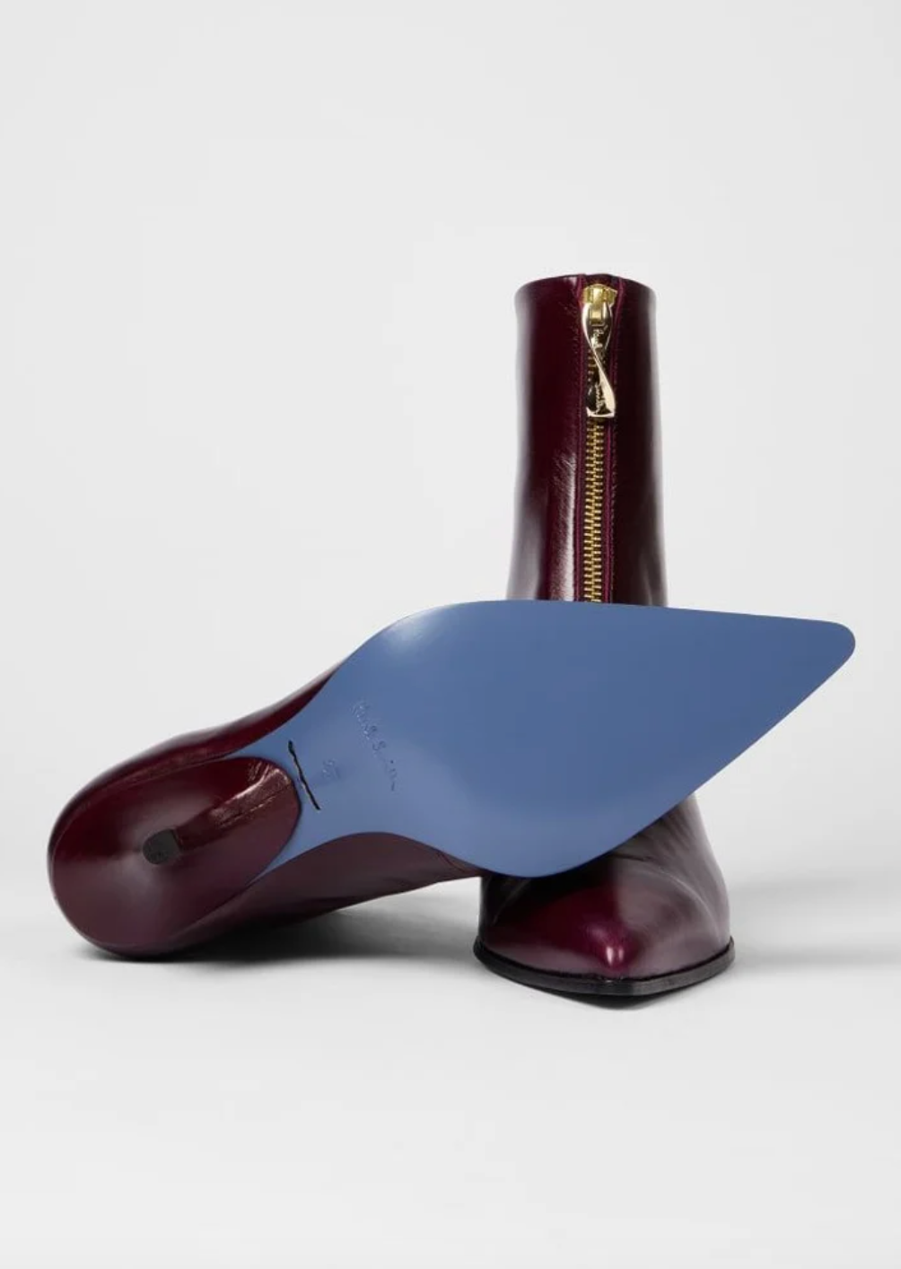 A pair of Paul Smith Winnie pointed-toe ankle boots in glossy burgundy leather with gold-tone side zippers and kitten heels, with blue soles available at The Shoe Gallery