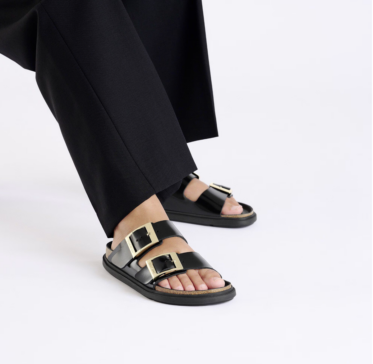 Model wearing black Birkenstock Arizona sandals with gold buckles and black bumper style soles