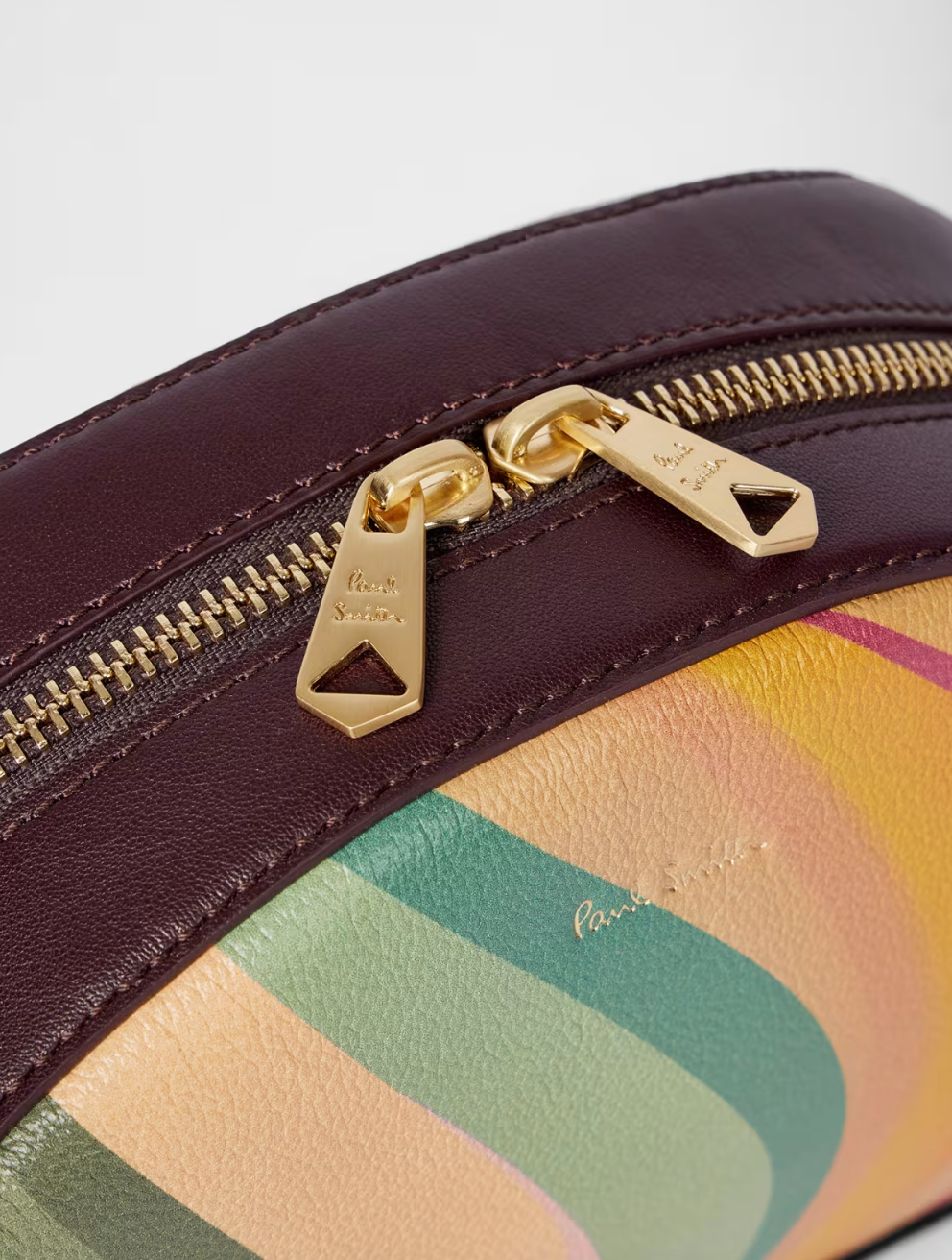 A Paul Smith dusky swirl  striped bag in a camera bag style. Centre gold coloured zip and deep burgundy across body strap, available at The Shoe  Gallery