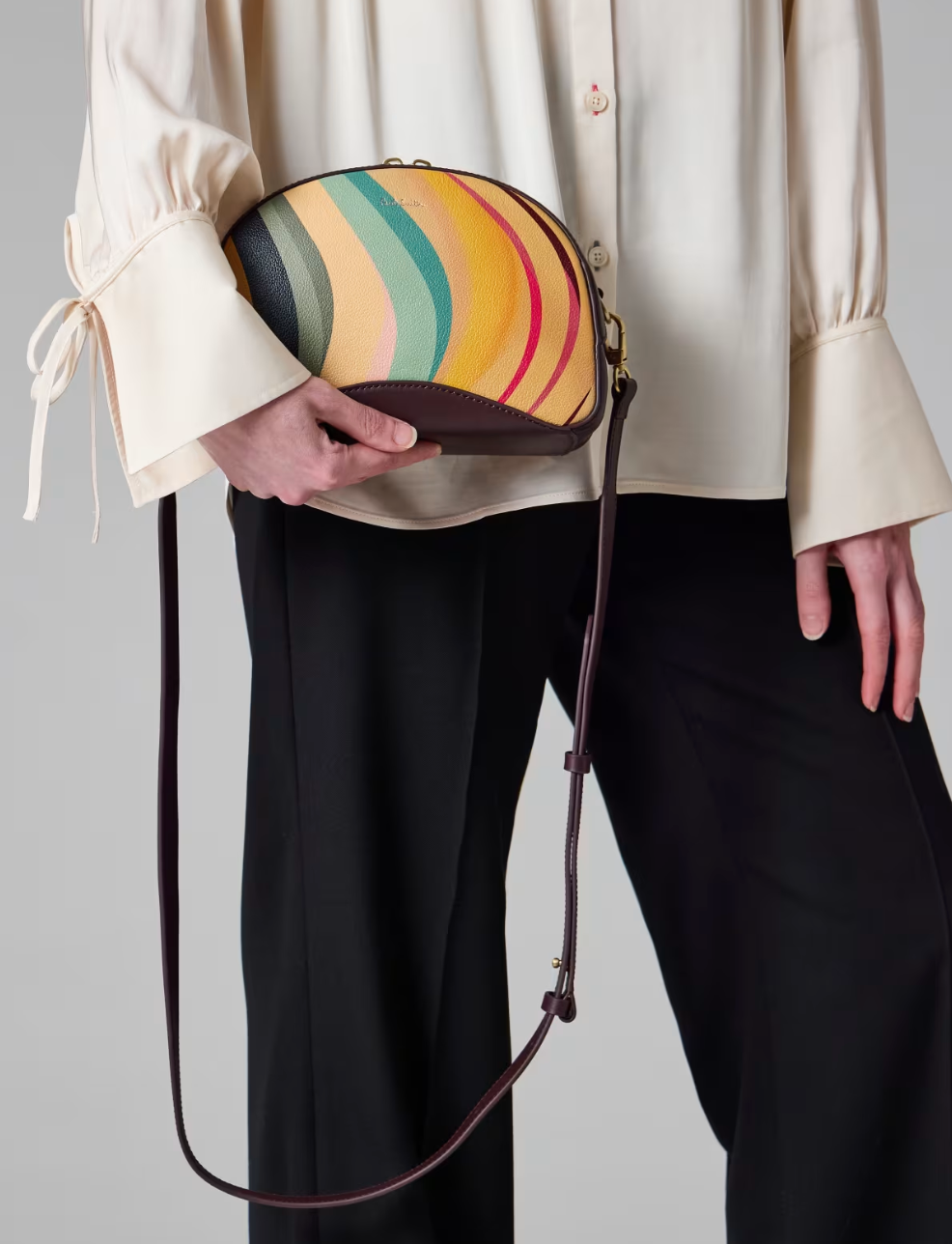 A Paul Smith dusky swirl  striped bag in a camera bag style. Centre gold coloured zip and deep burgundy across body strap, available at The Shoe  Gallery