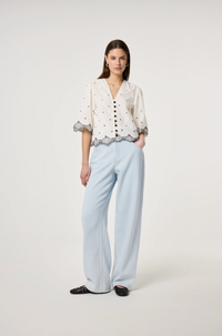 Model wears the Fabienne Chapot Tylera Blouse in ecru with small black polka dots and edged with embroidered fish at both the hemline and the three quarter sleeve edge. It has tiny black button central closure