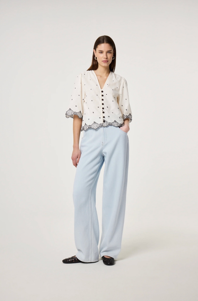 Model wears the Fabienne Chapot Tylera Blouse in ecru with small black polka dots and edged with embroidered fish at both the hemline and the three quarter sleeve edge. It has tiny black button central closure