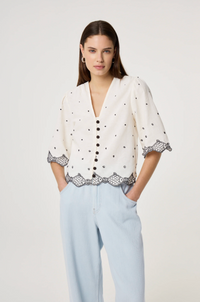 Model wears the Fabienne Chapot Tylera Blouse in ecru with small black polka dots and edged with embroidered fish at both the hemline and the three quarter sleeve edge. It has tiny black button central closure