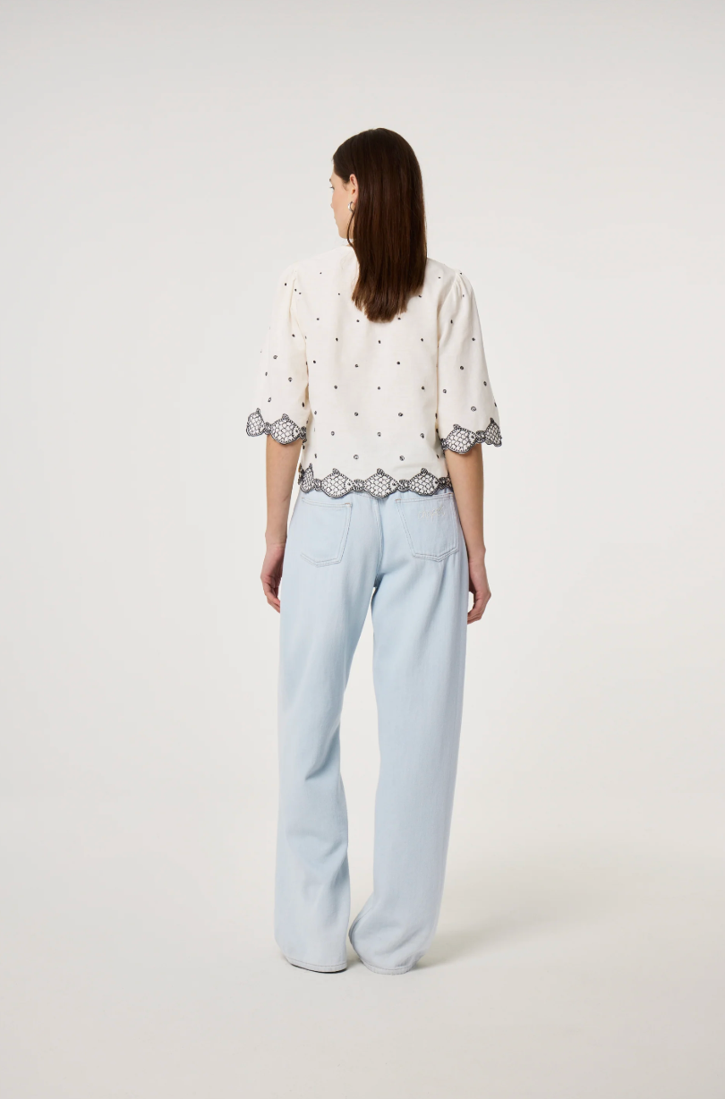 Model wears the Fabienne Chapot Tylera Blouse in ecru with small black polka dots and edged with embroidered fish at both the hemline and the three quarter sleeve edge. It has tiny black button central closure, back view