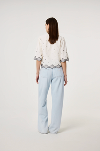 Model wears the Fabienne Chapot Tylera Blouse in ecru with small black polka dots and edged with embroidered fish at both the hemline and the three quarter sleeve edge. It has tiny black button central closure, back view